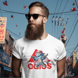 Bărbat cu barbă și ochelari de soare, purtând un tricou alb cu un design ce include un personaj animat albastru(Stitch) stil streetwear ținând două arme de jucărie, în fața unui fundal urban cu semne în limba coreeană și logo stilizat Adidas în roșu.