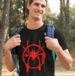 Tânăr zâmbitor purtând un tricou negru cu un design roșu reprezentând un păianjen stilizat, în stil graffiti, și un rucsac albastru pe umeri, într-un cadru natural cu copaci în fundal.