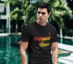 Un bărbat serios, cu păr scurt, stă în picioare și poartă un tricou negru cu text colorat. Pe tricou apare mesajul 'Dezbracă-te să vorbim,' scris în culori roșu și galben neon, împreună cu câteva stele decorative galbene. În fundal se observă un decor tro