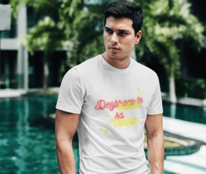 Un bărbat serios, cu păr scurt, stă în picioare și poartă un tricou alb cu text colorat. Pe tricou apare mesajul 'Dezbracă-te să vorbim,' scris în culori roșu și galben neon, împreună cu câteva stele decorative galbene. În fundal se observă un decor tropi