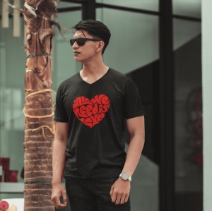 Bărbat purtând ochelari de soare și un tricou negru cu un design roșu în formă de inimă, conținând textul 'All we need is love', stând lângă un trunchi de copac învelit în sfoară.
