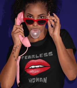 Fată purtând un tricou negru cu designul 'Fearless Woman' și buze roșii grafice, vorbind la un telefon roz vintage, cu ochelari de soare roșii și făcând un balon de gumă de mestecat, pe un fundal albastru închis.