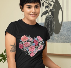 Fată zâmbitoare purtând un tricou negru cu un design floral colorat în formă de inimă, într-un cadru interior decorat artistic, având un tatuaj pe braț.