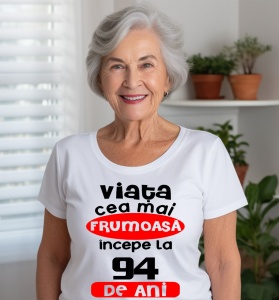 Femeie care poartă un tricou alb personalizat cu mesajul: ''Viata cea mai frumoasa incepe la 94 de ani''.