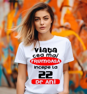 Femeie care poartă un tricou alb personalizat cu mesajul: ''Viata cea mai frumoasa incepe la 22 de ani''.