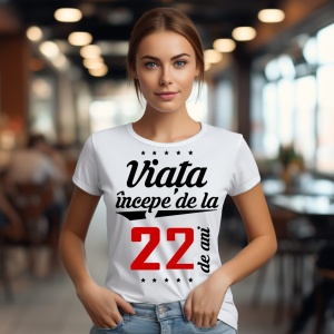 O femeie purtând un tricou alb cu textul  'Viața începe de la 22 de ani'. Fundal din lemn cu diferite nuanțe de maro și verde.