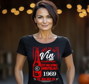 Femeie zâmbitoare purtând un tricou negru cu un mesaj în română despre vin, în care se menționează că este ca un vin bun care devine mai nobil cu vârsta, îmbuteliat în 1969, cel mai bun an.