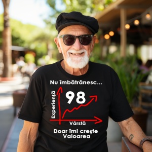 Un bărbat în vârstă, purtând ochelari de soare și o beretă neagră, zâmbind, și îmbrăcat într-un tricou negru cu mesajul: „Nu îmbătrânesc... Doar îmi crește valoarea”, alături de un grafic care indică vârsta de 98 de ani pe axa vârstei și experienței. Bărb