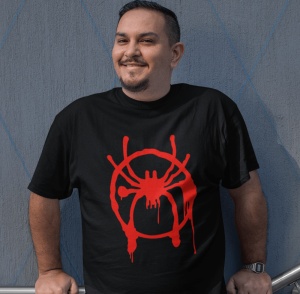 Bărbat zâmbitor purtând un tricou negru cu un design roșu reprezentând un păianjen stilizat, în stil graffiti, sprijinit de o balustradă, pe un fundal cu perete texturat și linii diagonale albastre.