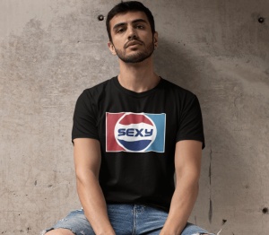 Un bărbat purtând un tricou negru cu un design inspirat de logo-ul Pepsi, dar cu textul 'Sexy' în centru, pozând într-un mediu minimalist și purtând pantaloni scurți din denim.