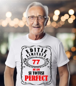 Un bărbat purtând un tricou alb cu mesajul: „Ediție limitată, 77 de ani și totuși perfect”. Bărbatul afișează o atitudine veselă și pozitivă.