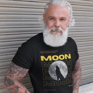 Un bărbat cu barbă albă și păr ondulat, purtând un tricou negru cu un design care prezintă o lună plină și o siluetă de lup, alături de textul 'MOON' scris în galben. Bărbatul are tatuaje pe brațe și stă în fața unei uși metalice rulante, adăugând un cont