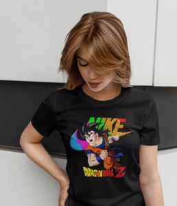 Femeie purtând un tricou negru cu un design colorat ce include un personaj din 'Dragon Ball Z' și textul 'Nike,' pozând în fața unui perete modern, cu privirea în jos.