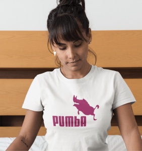 Femeie cu părul prins și breton, purtând cercei în formă de inimă, îmbrăcată într-un tricou alb cu un design roz ce prezintă silueta unui facocer și textul 'PUMBA'. Femeia se uită în jos cu o expresie calmă și relaxată. Fundalul este parțial din lemn, ofe