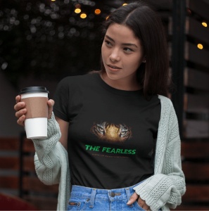 Fată purtând un tricou negru cu un design grafic ce prezintă ochii unui tigru și textul 'THE FEARLESS', ținând o cană de cafea și purtând un cardigan, într-un mediu exterior iluminat.