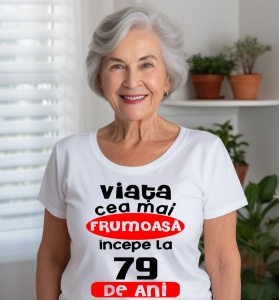 Femeie care poartă un tricou alb personalizat cu mesajul: ''Viata cea mai frumoasa incepe la 79 de ani''.
