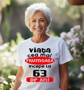Femeie care poartă un tricou alb personalizat cu mesajul: ''Viata cea mai frumoasa incepe la 63 de ani''.