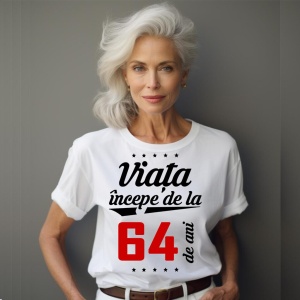 O femeie purtând un tricou alb cu textul  'Viața începe de la 64 de ani'. Fundal din lemn cu diferite nuanțe de maro și verde.