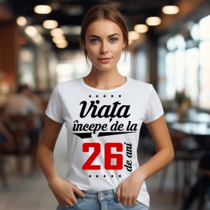 O femeie purtând un tricou alb cu textul  'Viața începe de la 26 de ani'. Fundal din lemn cu diferite nuanțe de maro și verde.