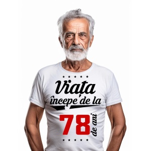 Bărbat în vârstă cu barbă albă, purtând un tricou alb cu mesajul 'Viața începe de la 78 de ani', pe un fundal alb simplu.