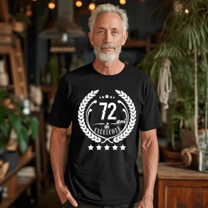 Un bărbat zâmbitor purtând un tricou negru cu textul ''72 de ani de excelență'', înconjurat de o coroană de lauri.