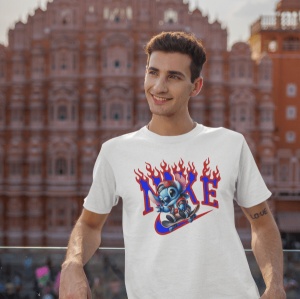 Tânăr zâmbitor purtând un tricou alb cu un design ce include un personaj animat albastru(Stitch), stilizat cu elemente de flăcări și un logo stilizat Nike. Fundalul arată o clădire arhitecturală tradițională, de culoare cărămizie, într-un stil istoric.