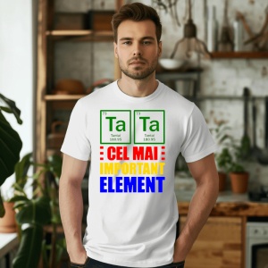 Bărbat serios purtând un tricou alb cu design bazat pe tabelul periodic, evidențiind Tantal (Ta) și mesajul în culori roșu, galben și albastru 'Cel mai important element', pozând într-o bucătărie decorată cu plante și rafturi din lemn.