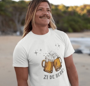 Bărbat cu părul lung blond și mustață, zâmbind și purtând un tricou alb pe care este imprimată o grafică cu două halbe de bere care se ciocnesc, cu spumă revărsându-se și câteva stele sclipitoare deasupra lor. Sub imagine, textul 'Zi de Bere!' este scris 