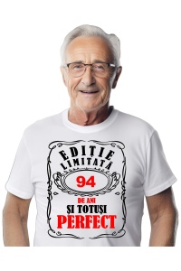 Un bărbat purtând un tricou alb cu mesajul: „Ediție limitată, 94 de ani și totuși perfect”. Bărbatul afișează o atitudine veselă și pozitivă.