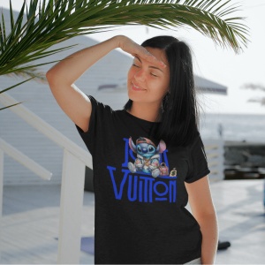 Femeie care poartă un tricou negru cu un design grafic ce combină un personaj animat(Stitch) și textul 'Louis Vuitton,' stând afară într-o zonă cu palmieri, la soare, și acoperindu-și ochii cu mâna.