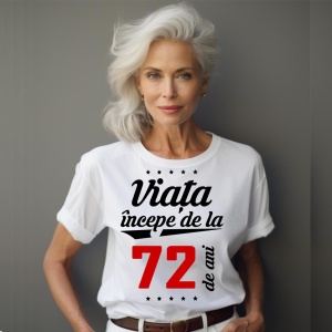 O femeie purtând un tricou alb cu textul  'Viața începe de la 72 de ani'. Fundal din lemn cu diferite nuanțe de maro și verde.