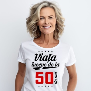 O femeie purtând un tricou alb cu textul  'Viața începe de la 50 de ani'. Fundal din lemn cu diferite nuanțe de maro și verde.