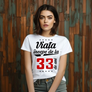 O femeie purtând un tricou alb cu textul  'Viața începe de la 33 de ani'. Fundal din lemn cu diferite nuanțe de maro și verde.