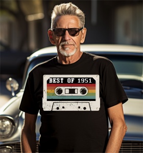 Un bărbat zâmbitor cu păr grizonat purtând un tricou negru cu o imagine stilizată a unei casete audio și textul ''Best of 1951''.