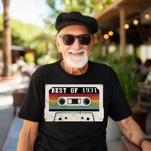 Un bărbat zâmbitor cu păr grizonat purtând un tricou negru cu o imagine stilizată a unei casete audio și textul ''Best of 1931''.