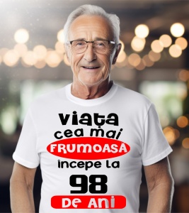Un bărbat purtând un tricou alb cu textul ''Viața cea mai frumoasă începe la 98 de ani''.