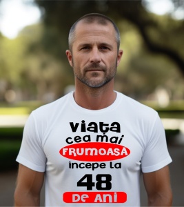 Un bărbat purtând un tricou alb cu textul ''Viața cea mai frumoasă începe la 48 de ani''.
