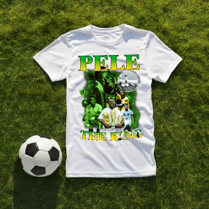 Tricou alb cu un design dedicat lui Pelé, incluzând imagini ale fotbalistului și textul 'Pelé The King', așezat pe iarbă alături de o minge de fotbal.