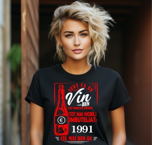 Femeie zâmbitoare purtând un tricou negru cu un mesaj în română despre vin, în care se menționează că este ca un vin bun care devine mai nobil cu vârsta, îmbuteliat în 1991, cel mai bun an.