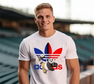 Bărbat tânăr și zâmbitor purtând un tricou alb cu un design colorat, ce include personaje animate(KungFu Panda Po) și un logo reinterpretat, pozând pe un stadion gol.