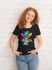 Femeie cu păr roșcat și creț purtând un tricou negru cu un design colorat ce include un personaj stilizat(Super Buddy) și un logo abstract, zâmbind și pozând în fața unui perete alb cu textură de cărămidă.