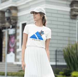 Femeie purtând un tricou alb cu un design al unui triunghi albastru și un personaj animat albastru(Stitch), care iese parțial din spatele triunghiului. Sub design apare textul 'PEACE'. Femeia poartă și o șapcă deschisă la culoare și o fustă albă, într-un 