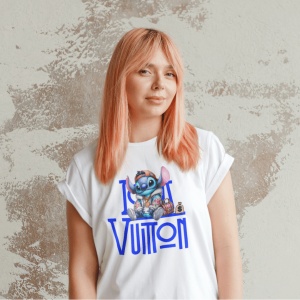 Femeie cu păr roz purtând un tricou alb cu un design grafic ce înfățișează un personaj animat(Stitch) și textul 'Louis Vuitton,' pozând în fața unui perete cu textură abstractă.