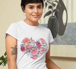 Fată zâmbitoare purtând un tricou alb cu un design floral colorat în formă de inimă, într-un cadru interior decorat artistic, având un tatuaj pe braț.