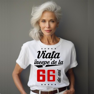 O femeie purtând un tricou alb cu textul  'Viața începe de la 66 de ani'. Fundal din lemn cu diferite nuanțe de maro și verde.