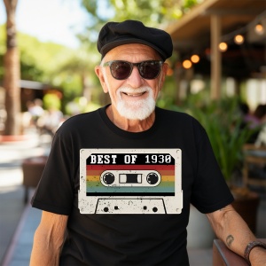 Un bărbat zâmbitor cu păr grizonat purtând un tricou negru cu o imagine stilizată a unei casete audio și textul ''Best of 1930''.