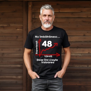 Un bărbat cu barbă albă purtând un tricou negru cu mesajul: „Nu îmbătrânesc... Doar îmi crește valoarea” și un grafic care indică vârsta de 48 de ani pe axa vârstei și experienței. Bărbatul se află într-un cadru simplu, cu un fundal întunecat.