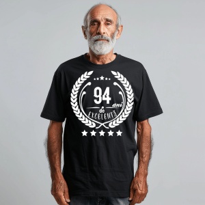 Un bărbat zâmbitor purtând un tricou negru cu textul ''94 de ani de excelență'', înconjurat de o coroană de lauri.