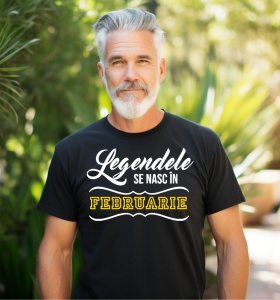 Un bărbat cu păr și barbă grizonate, purtând un tricou negru cu mesajul: „Legendele se nasc în Februarie”. Bărbatul se află într-un cadru exterior, înconjurat de vegetație verde.