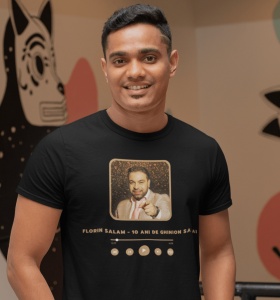 Un bărbat zâmbitor poartă un tricou negru cu un design inspirat de un player muzical, prezentând o fotografie a cântărețului Florin Salam și titlul piesei '10 Ani de Ghinion să Ai' scris dedesubt.